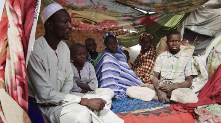 Mohamed Liman (à gauche) et sa famille dans leur abri de fortune dans le camp de déplacés de Teachers Village, à Maiduguri (État de Borno). Mohamed est venu de Cross Kauwa, à plus de 100 km au nord-est de Maiduguri, avec sa mère âgée, sa femme et leurs huit enfants. Le camp est surpeuplé suite aux nombreuses nouvelles arrivées dues à une multiplication des attaques dans l’État. La majeure partie des personnes récemment déplacées se sont installées à Teachers Village, mettant les ressources du camp à rude épreuve.