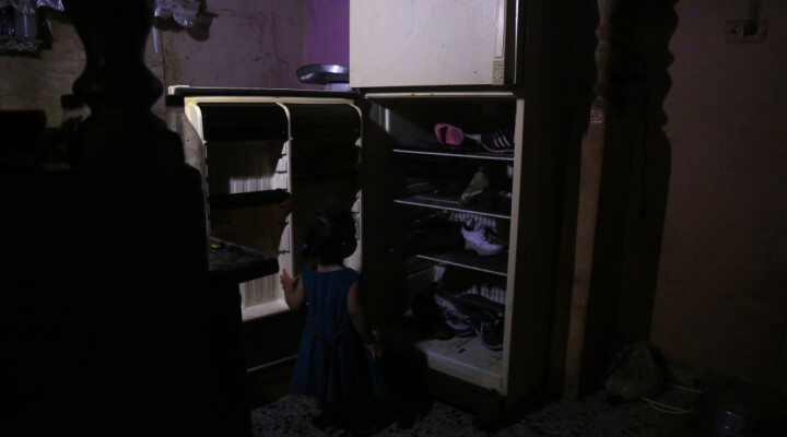 A girl is looking at a fridge without power used as a shoe storage space