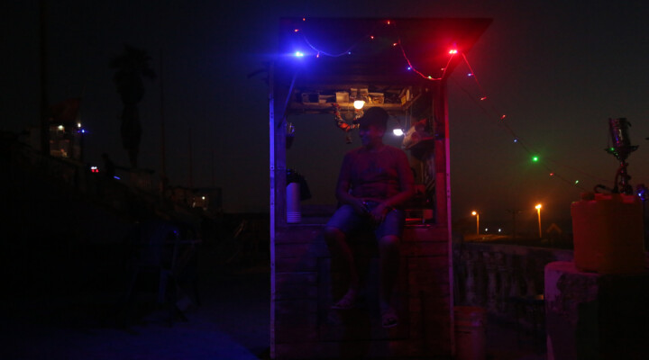 A street vendor next to his stand during the night in Gaza which us lit by LED lights.